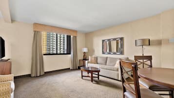 A hotel room with a sofa, a dining table, a TV, and a window with curtains.