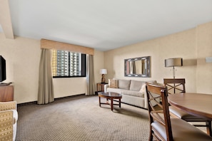 A hotel room with a sofa, a dining table, a TV, and a window with curtains. - The Carriage House (Las Vegas)