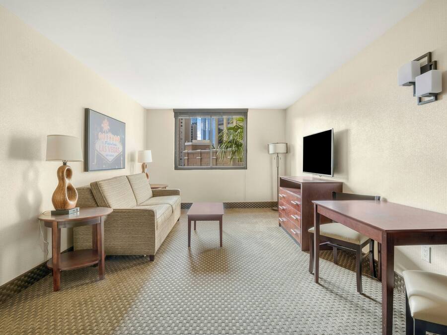 Een hotelkamer met een bank, een klein tafeltje, een bureau, een televisie en een raam met uitzicht op gebouwen.