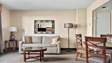 Una habitación de hotel con un sofá, una mesa de centro redonda, una lámpara de pie, una mesa de comedor con sillas y un espejo en la pared.