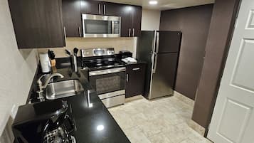A modern kitchen with dark cabinetry, stainless steel appliances, and a black countertop.