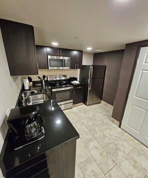 A modern kitchen with dark cabinetry, stainless steel appliances, and a black countertop.
