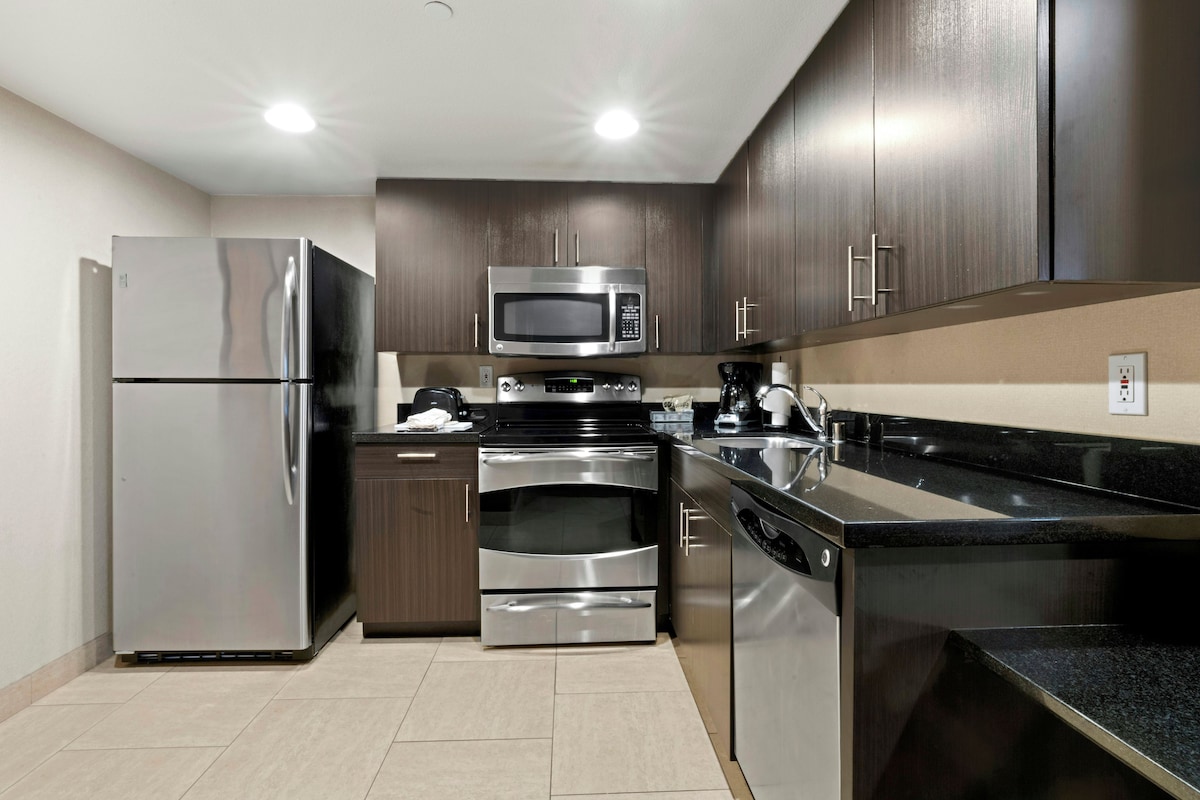 A modern kitchen with stainless steel appliances, dark wood cabinets, and a black granite countertop.