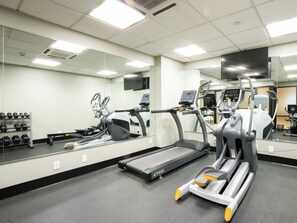 Una palestra con attrezzature per esercizi, un tapis roulant e uno specchio lungo la parete.