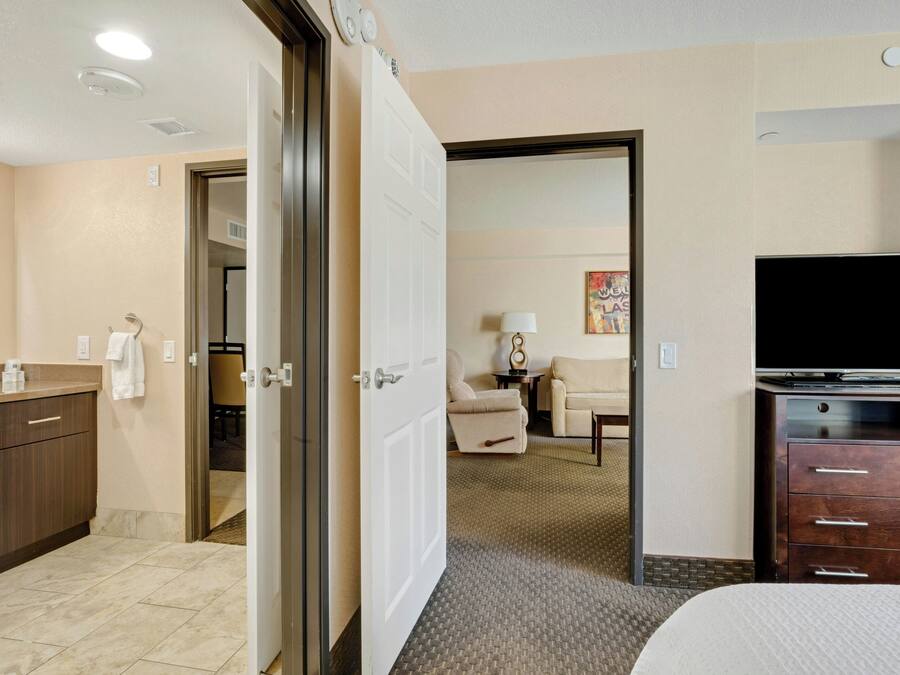 Quarto de hotel com cama, televisão, escrivaninha e banheiro.