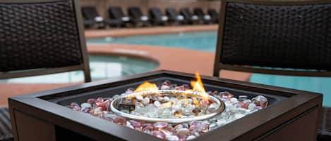 A poolside lounge area with a fire feature surrounded by chairs and umbrellas.