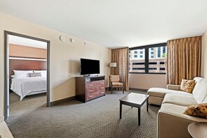 A hotel room with a bed, a TV, a sofa, a chair, and a desk. - The Carriage House (Las Vegas)