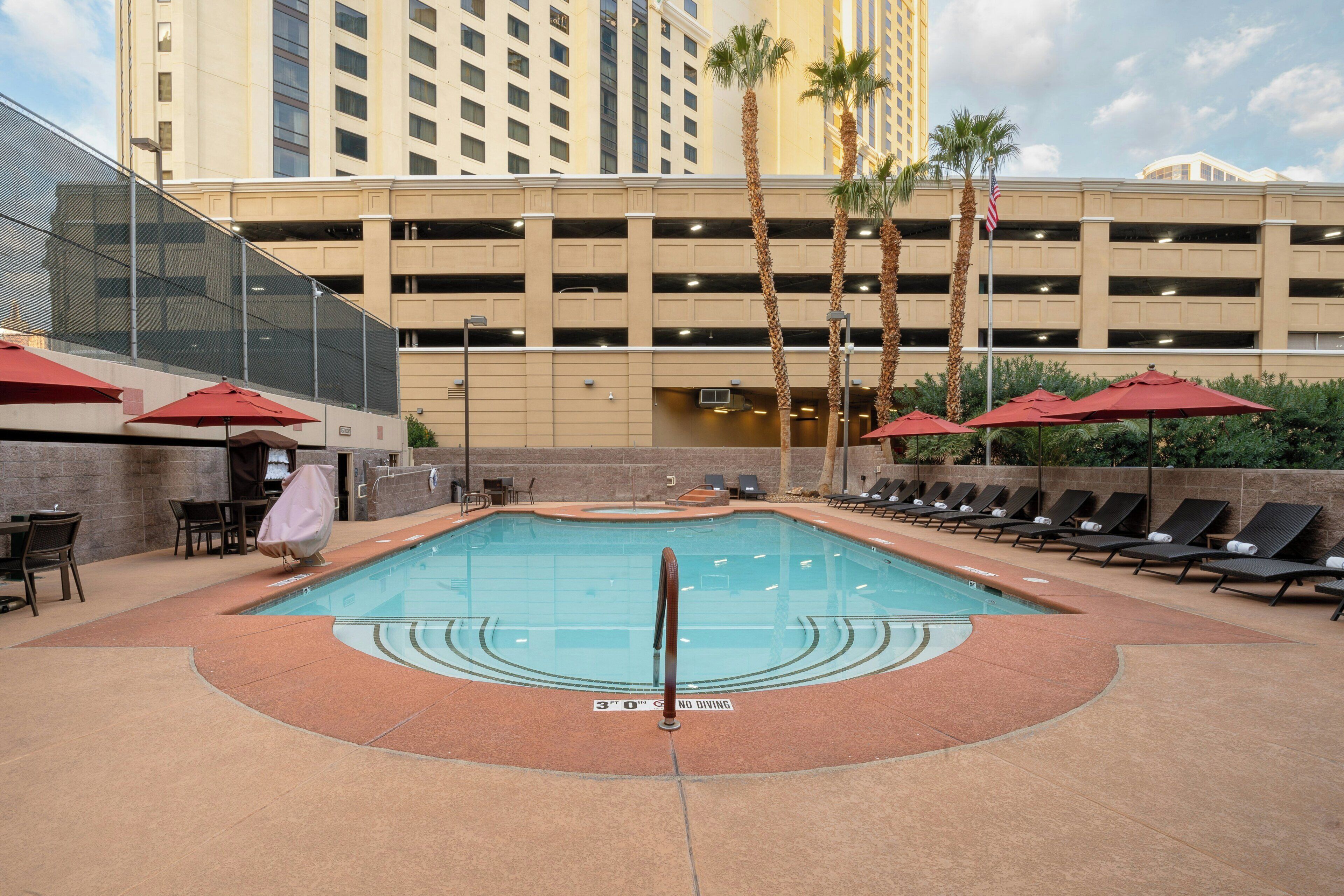 A hotel pool area with a clear water surface, sun loungers, and a no diving sign.