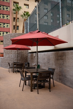 An outdoor patio with a table and chairs under a red umbrella, a stone wall, and a tall building in the background. - The Carriage House (Las Vegas)