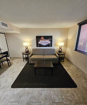 A living room with a sofa, two side tables, a coffee table, and a wall-mounted sign. - The Carriage House (Las Vegas)