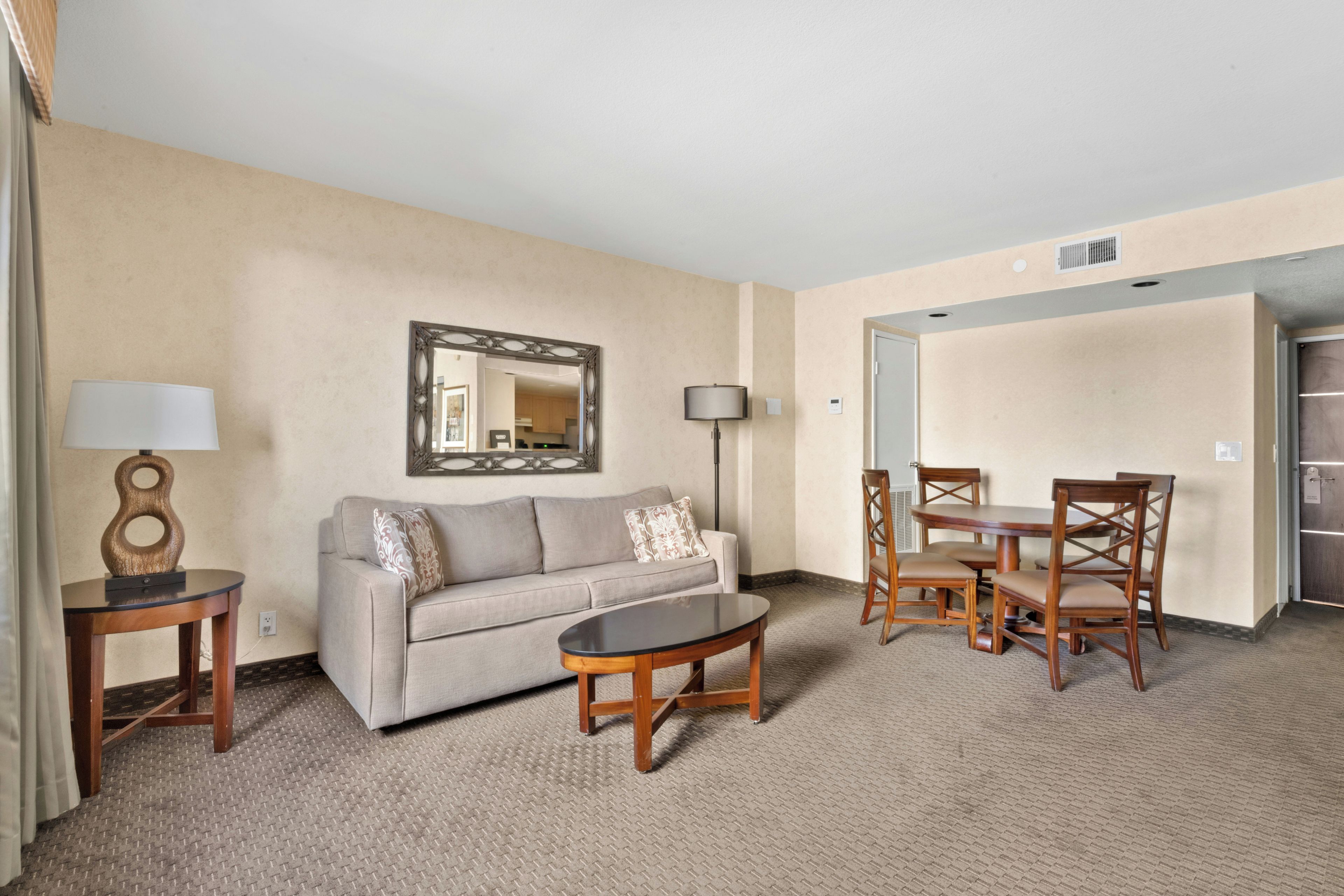 Une chambre d’hôtel avec un canapé, une table basse, une table à manger avec des chaises, une lampe et un miroir au mur.