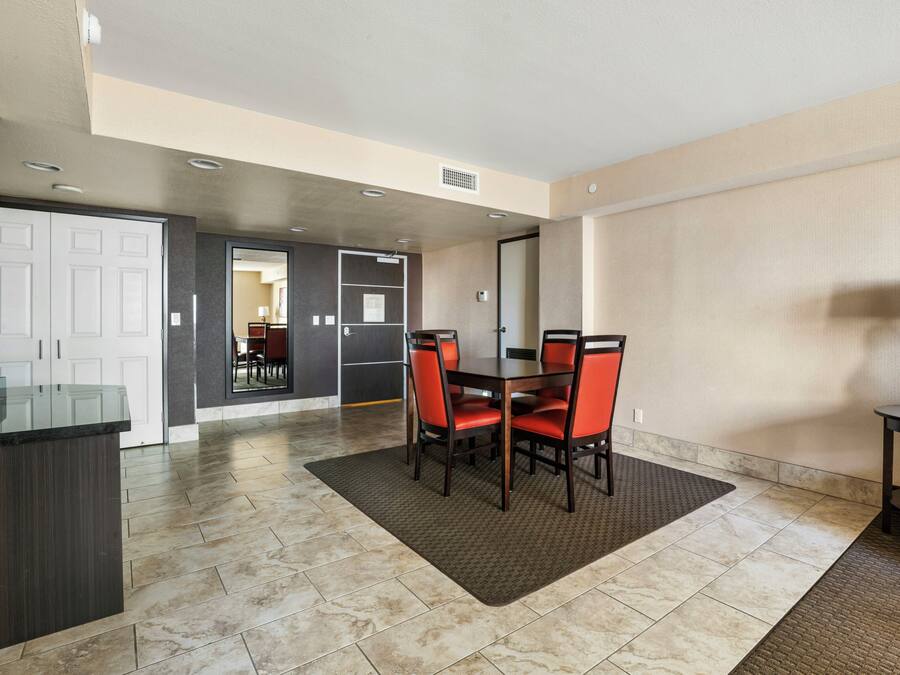 A hotel room with a dining area featuring a table and chairs, a kitchen area, and a bathroom visible through an open door.
