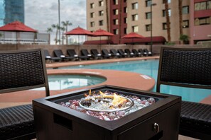 Un área junto a la piscina con sillones de descanso, una chimenea y la piscina.