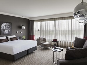 A modern hotel room with a large bed, a seating area with a chair and sofa, a small table with a wine glass and bottle, and a large window with curtains. - Pullman Melbourne Albert Park (Melbourne)