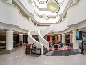 A spacious lobby with a central staircase, multiple seating areas, and a large digital screen. - Pullman Melbourne Albert Park (Melbourne)