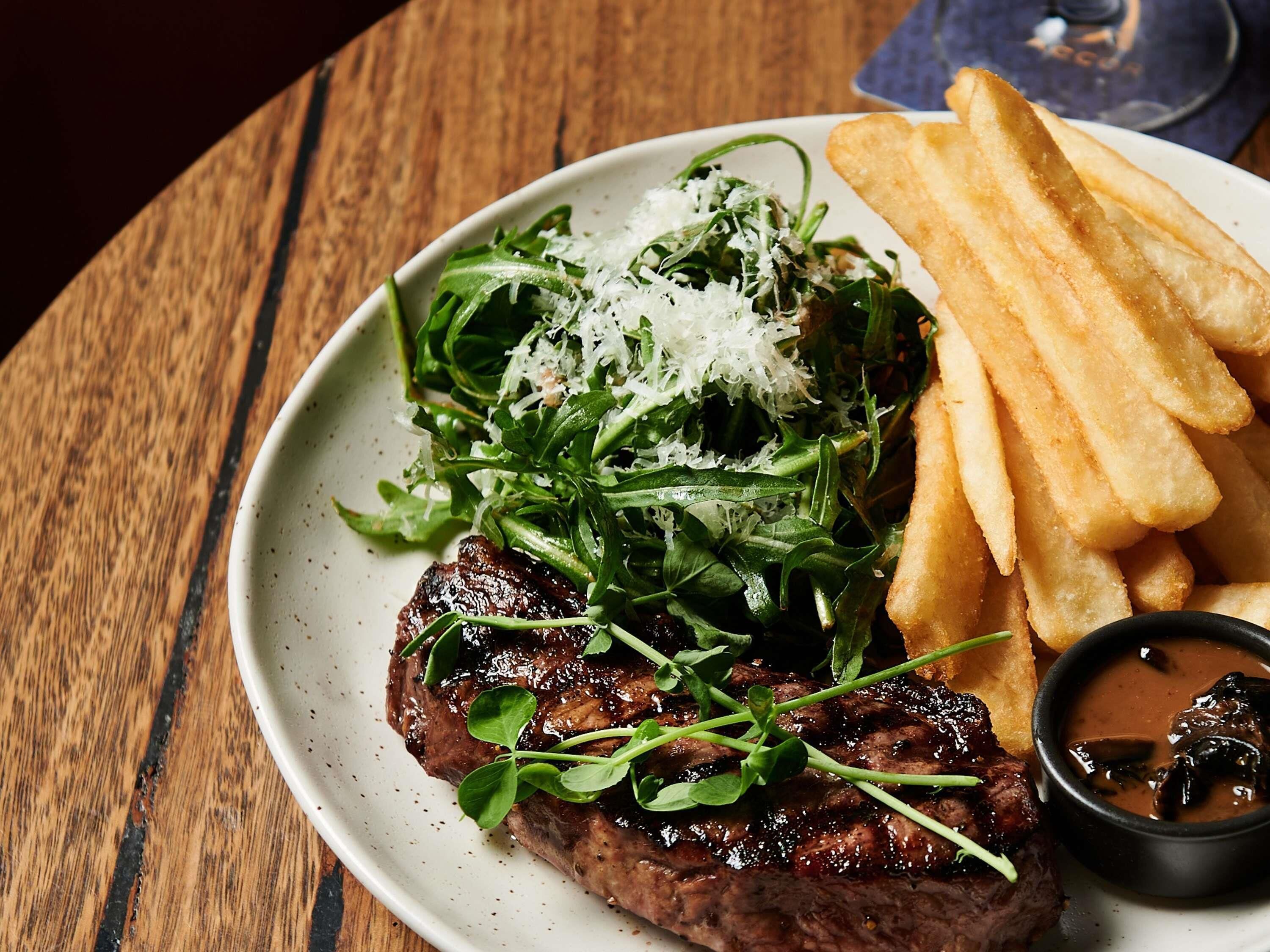 Ein Teller mit Steak, Pommes, Salat und Soße.