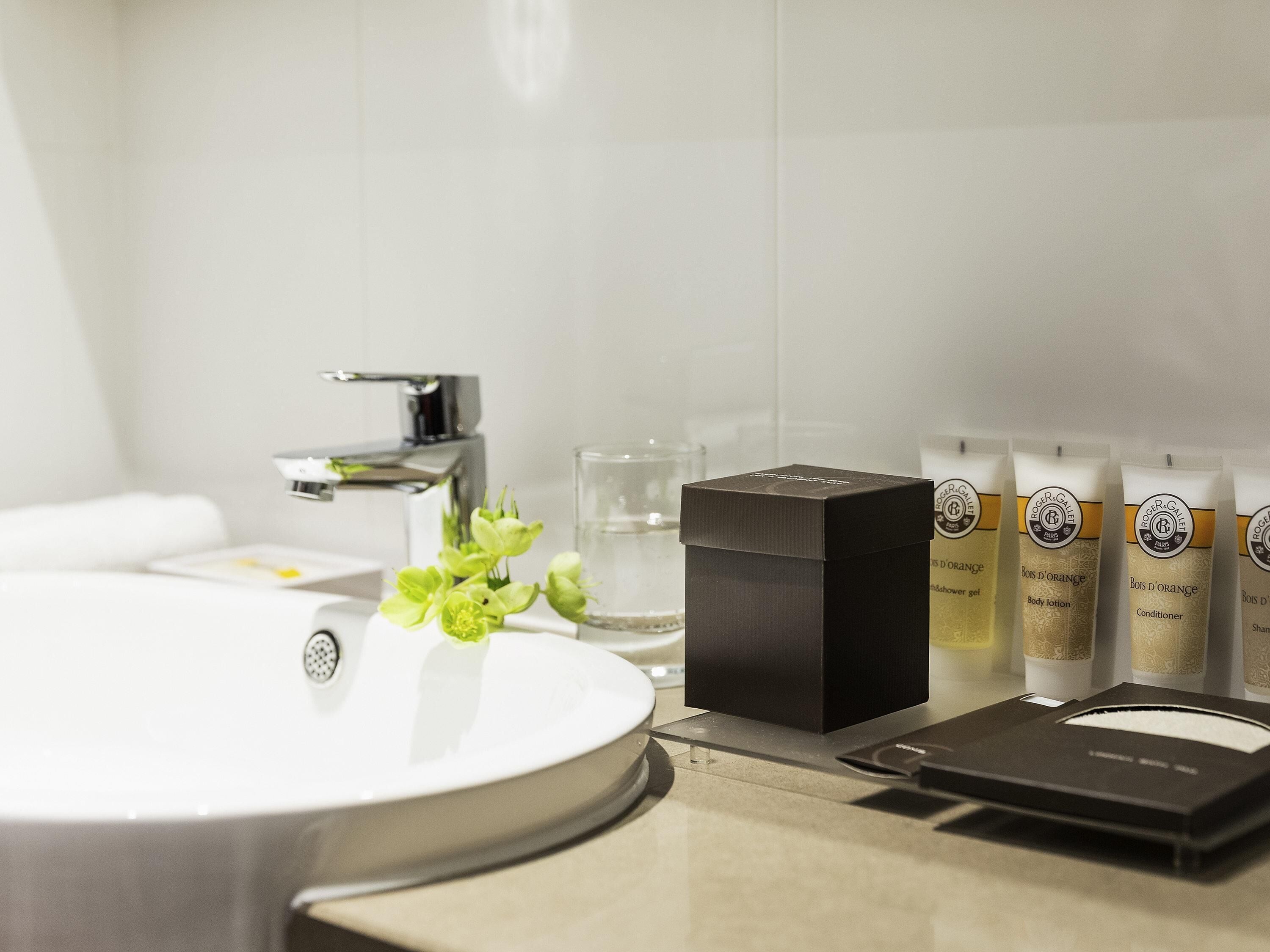 Un bany amb un lavabo blanc, una caixa negra i diversos productes de tocador sobre la superfície.