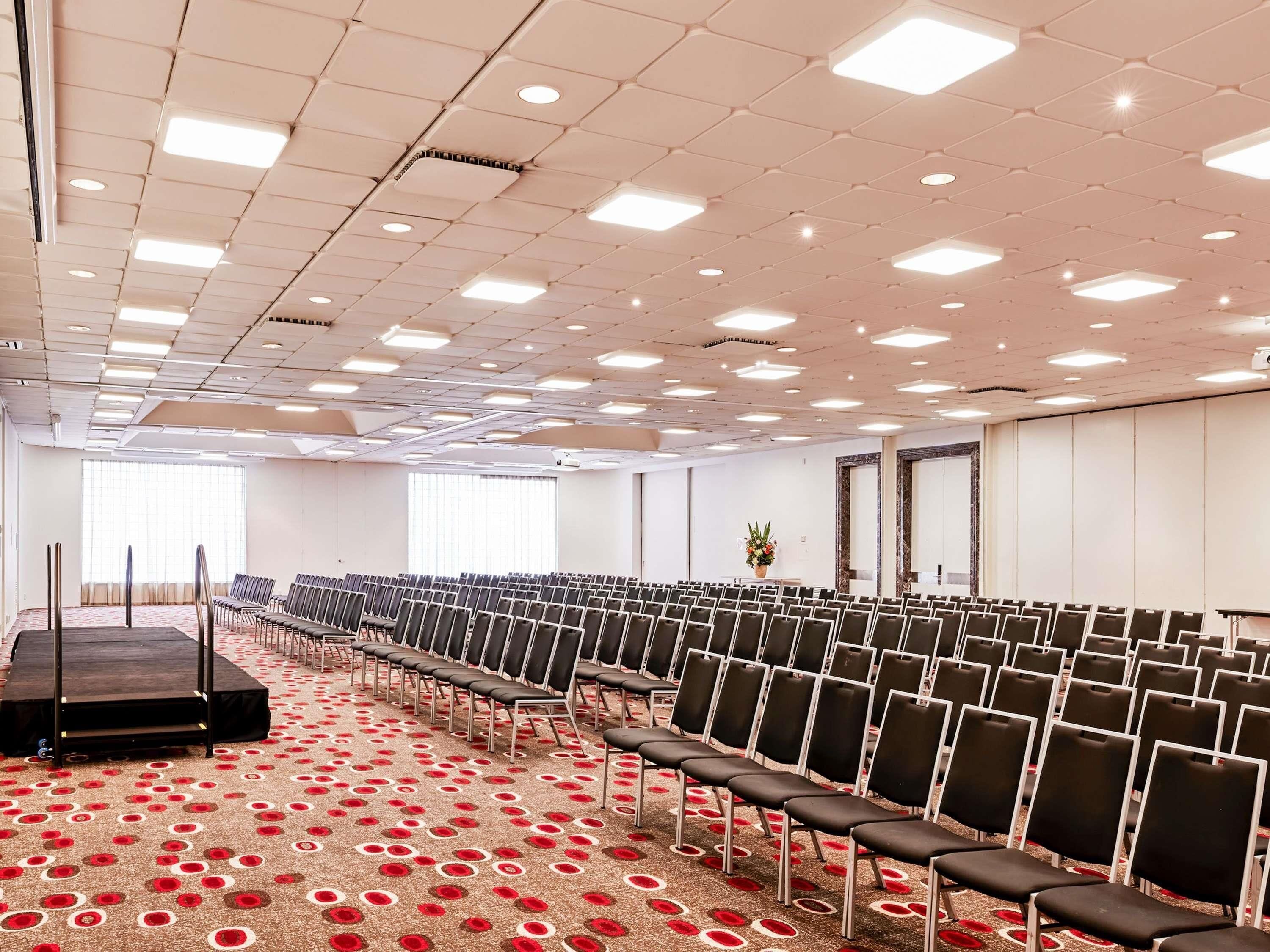 A conference room with rows of chairs, a stage, and a patterned carpet.