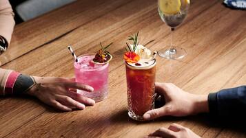 A wooden table with two drinks, one pink and one red, garnished with flowers and herbs.