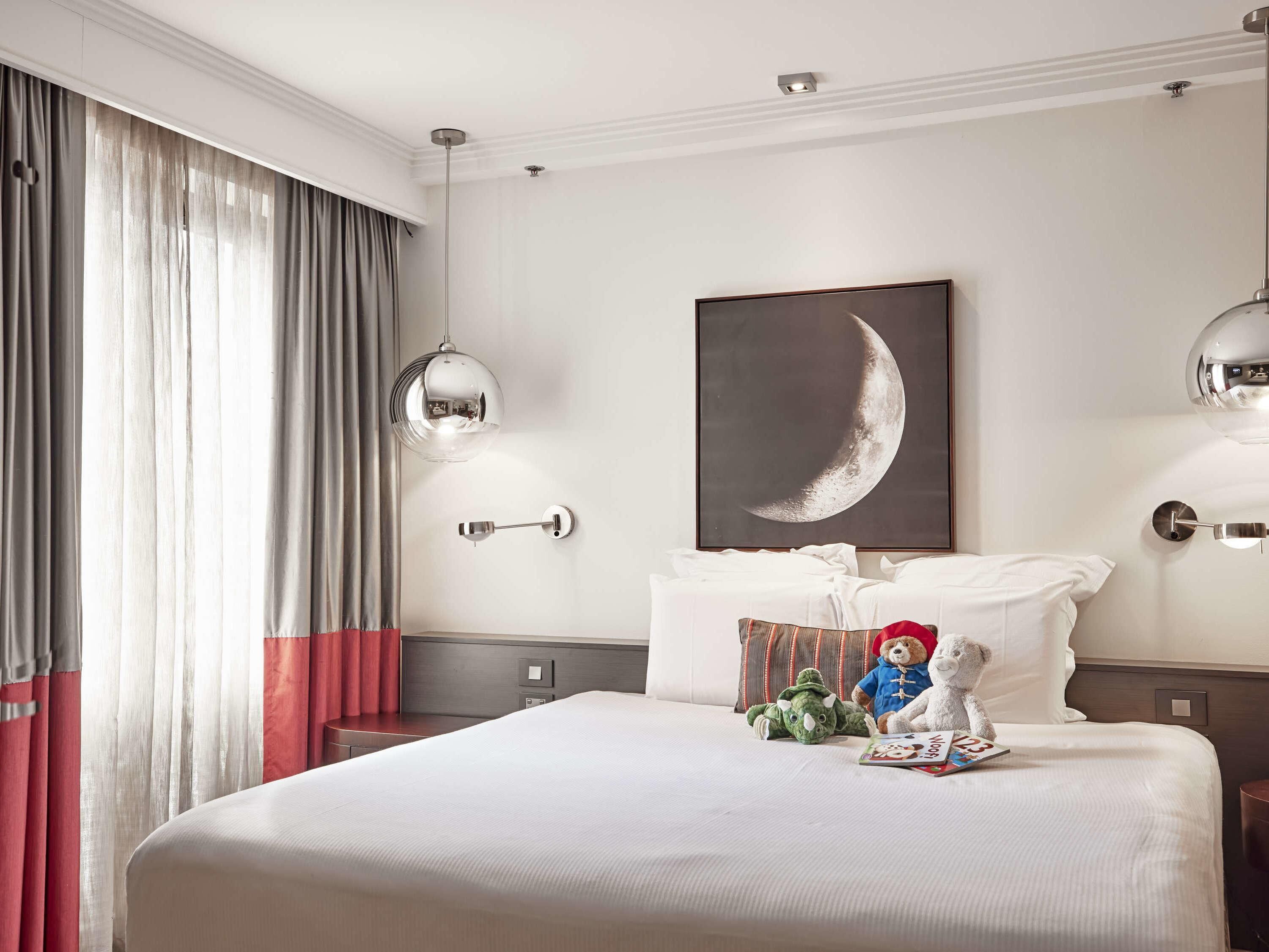 Una habitación de hotel con una cama grande, un cuadro de luna creciente colgado en la pared y dos lámparas de pared.
