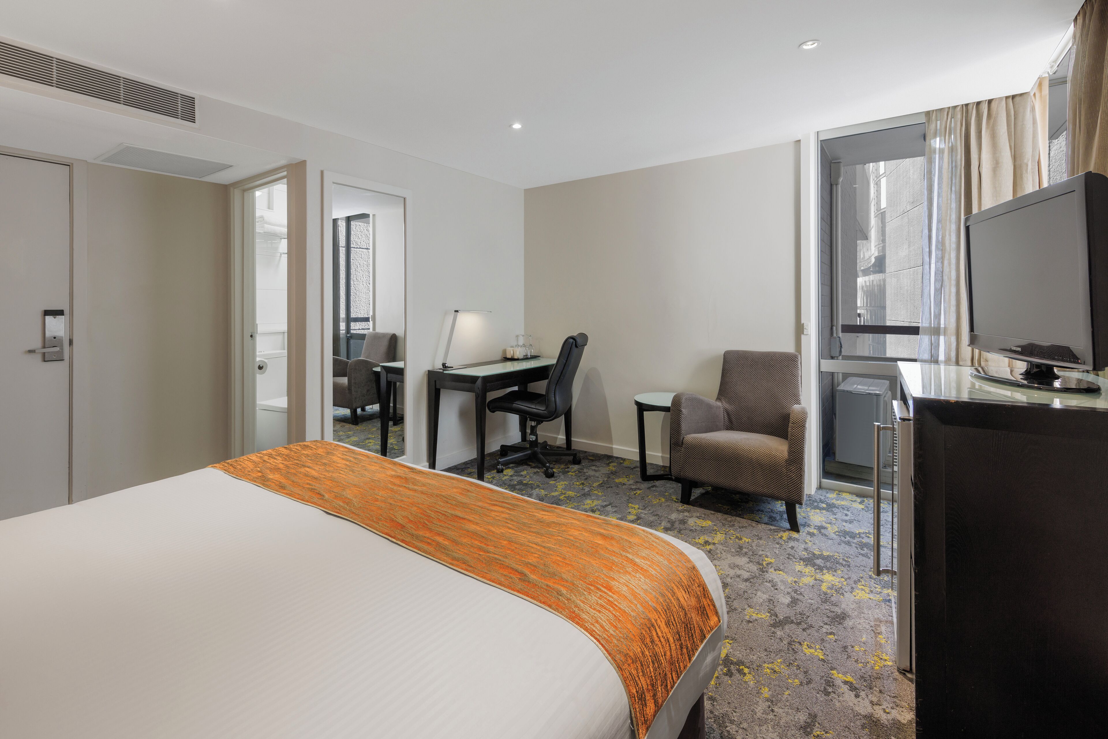 Una habitación de hotel con cama, escritorio, silla, televisor y un amplio ventanal.