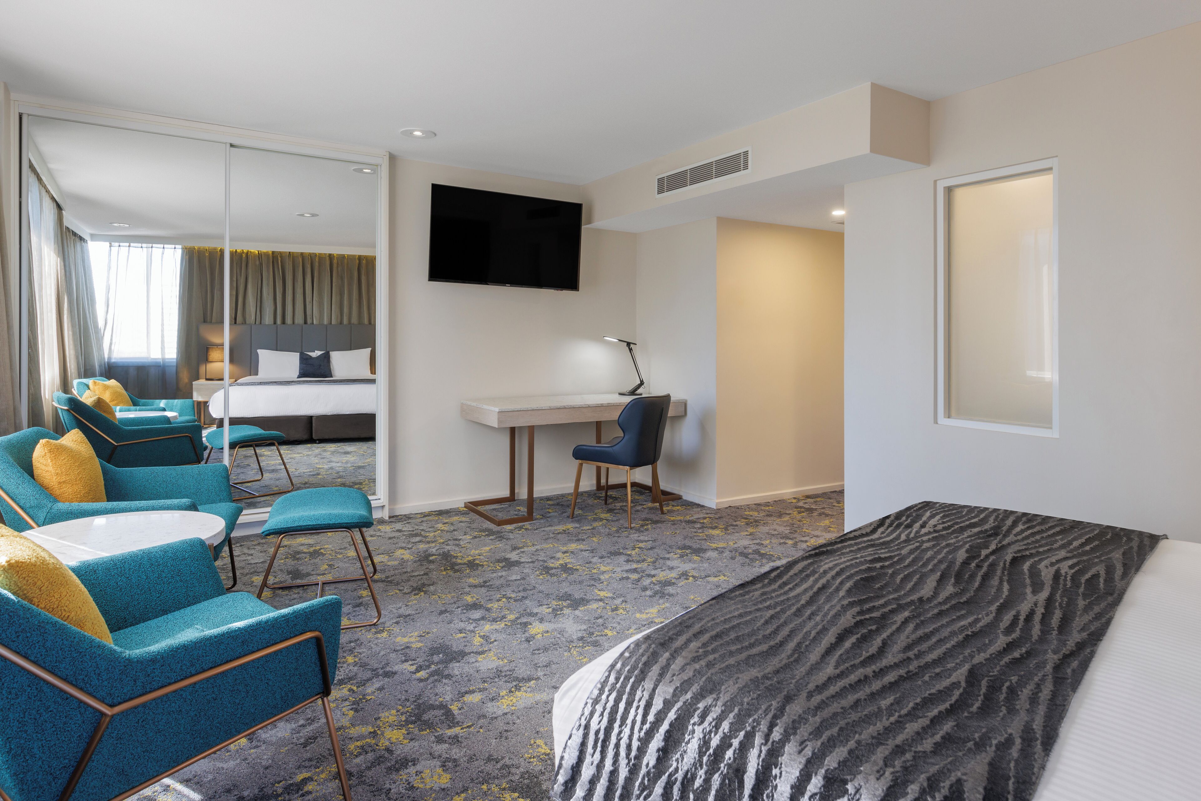 A hotel room with a bed, a desk, a chair, and a TV.