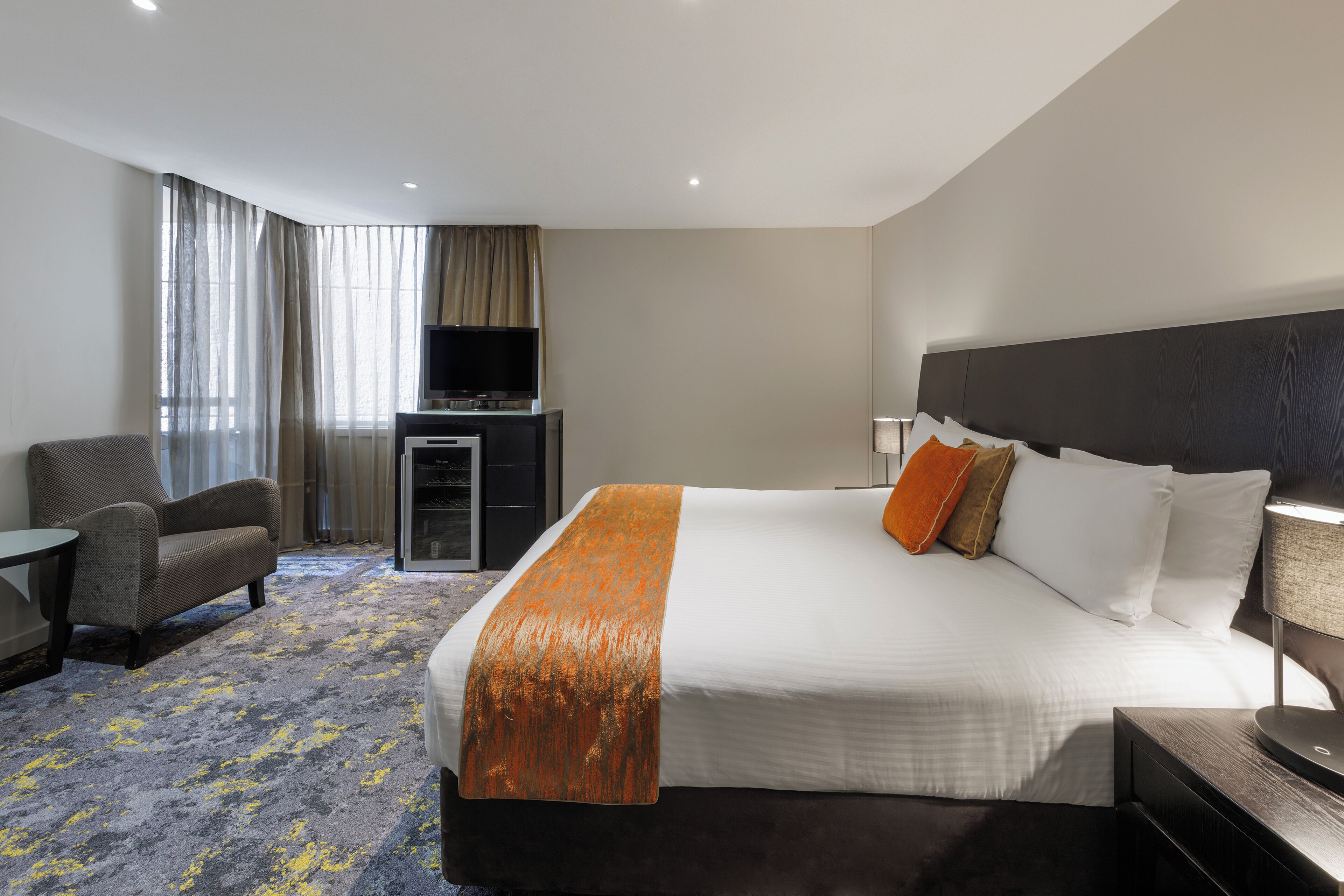 Habitación de hotel con una cama grande, una silla, un escritorio y un televisor.