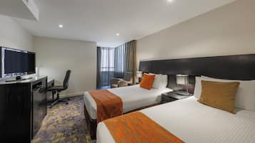 Habitación de hotel con dos camas, un escritorio con televisor, una silla y un ventanal con cortinas.