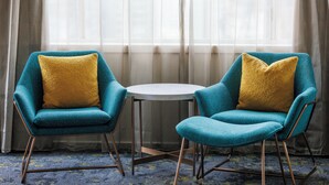 Dos sillones color turquesa con cojines color mostaza, una mesita redonda y una alfombra estampada azul.