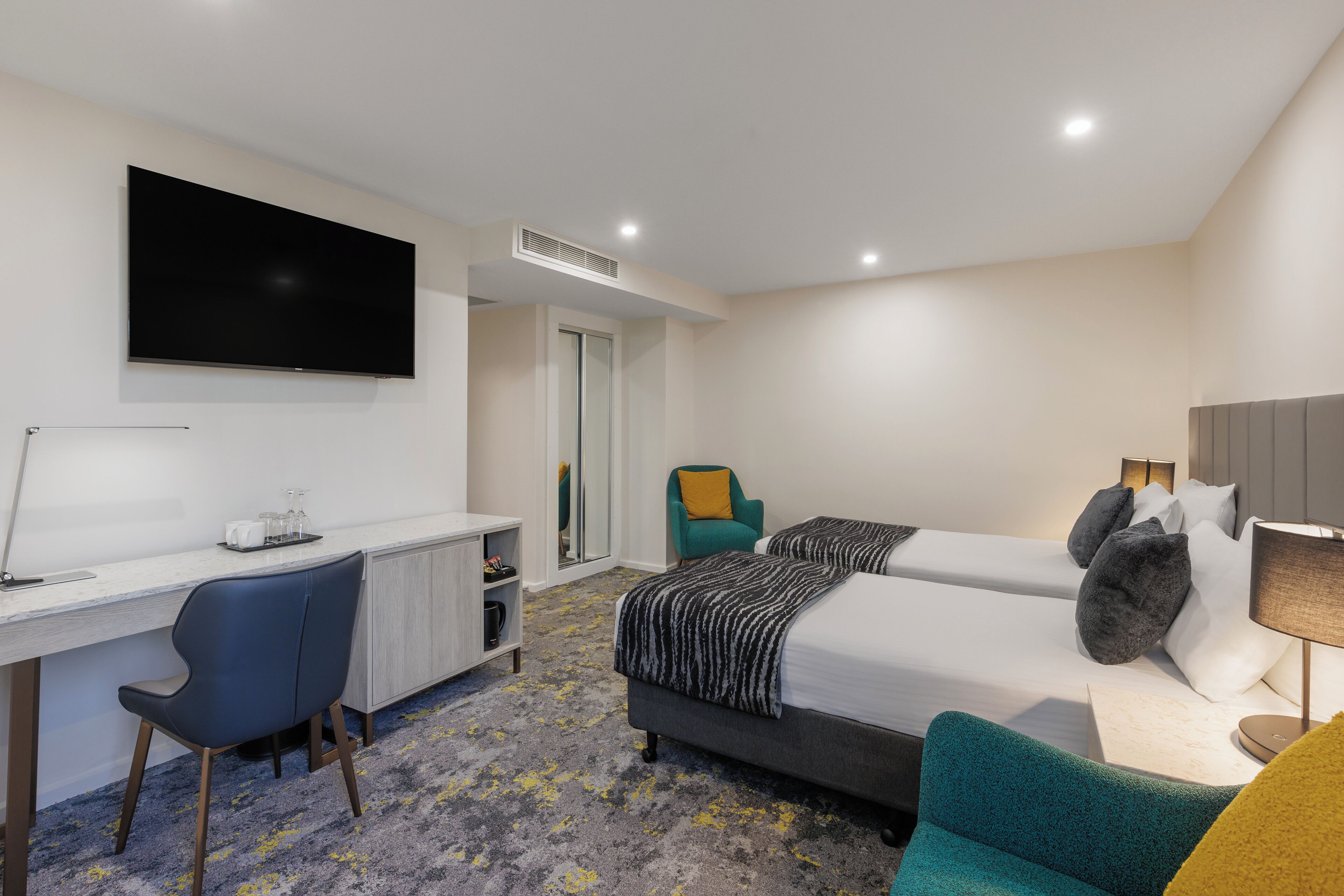 A hotel room with a bed, a desk, a chair, a TV, and a mirror.