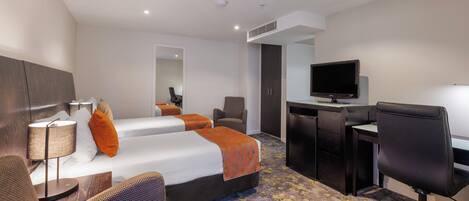 A hotel room with a bed, two bedside tables, a desk with a chair, a television, and a bathroom.