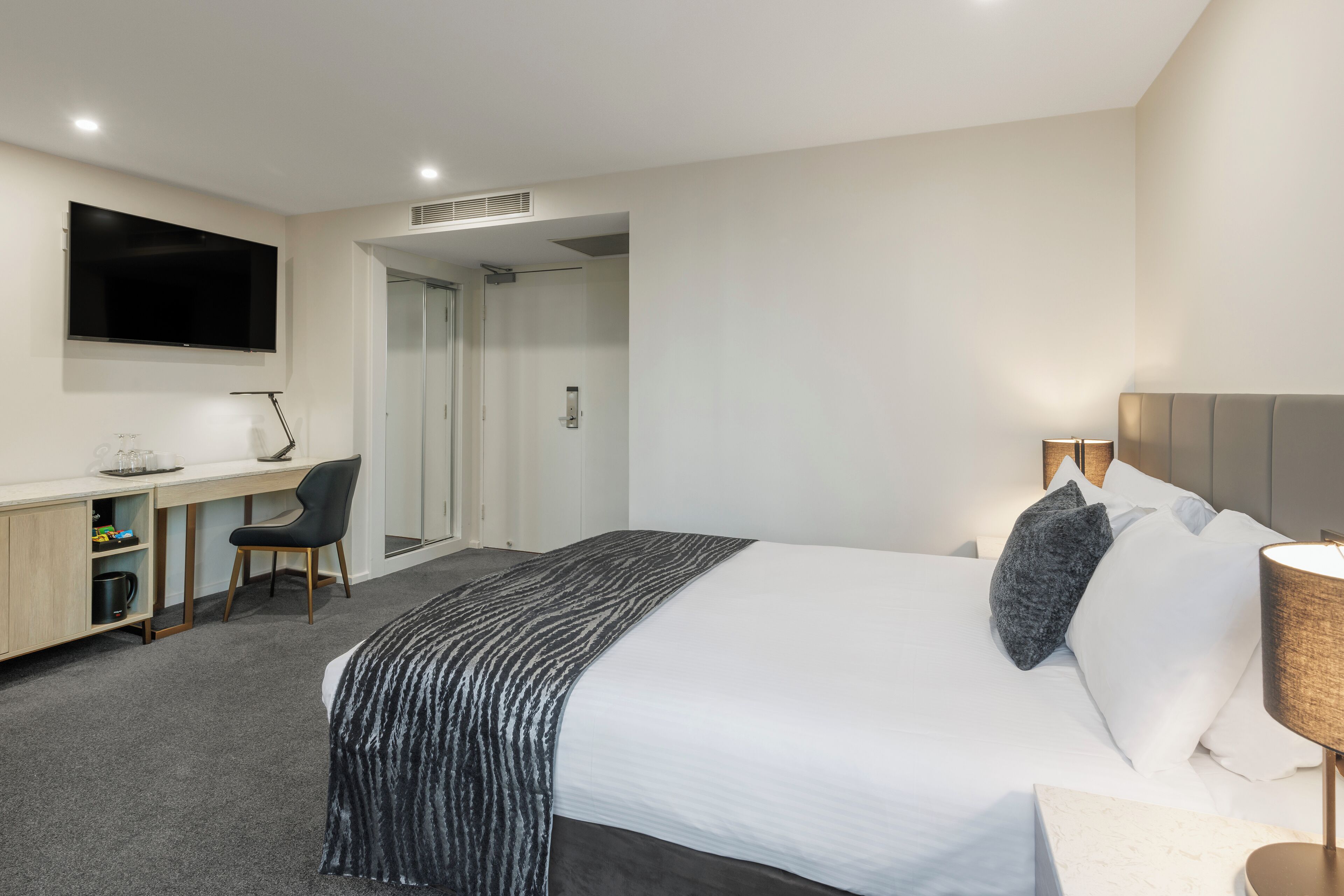 Ein Hotelzimmer mit Bett, Schreibtisch, Stuhl, Fernseher und Lampe.