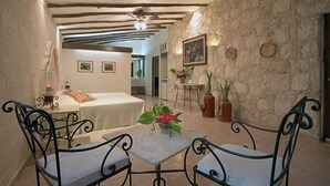 A cozy room with a bed, a small table with chairs, a ceiling fan, and a stone wall. - Hacienda Chichen Resort & Yaxkin Spa (Chichen Itza)