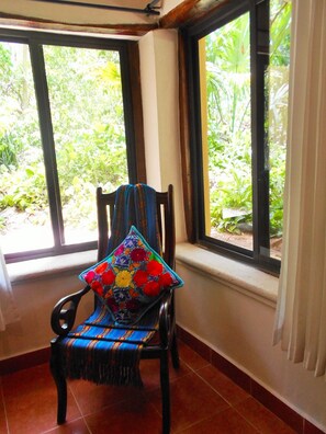 A chair with a colorful cushion in a room with large windows overlooking greenery.