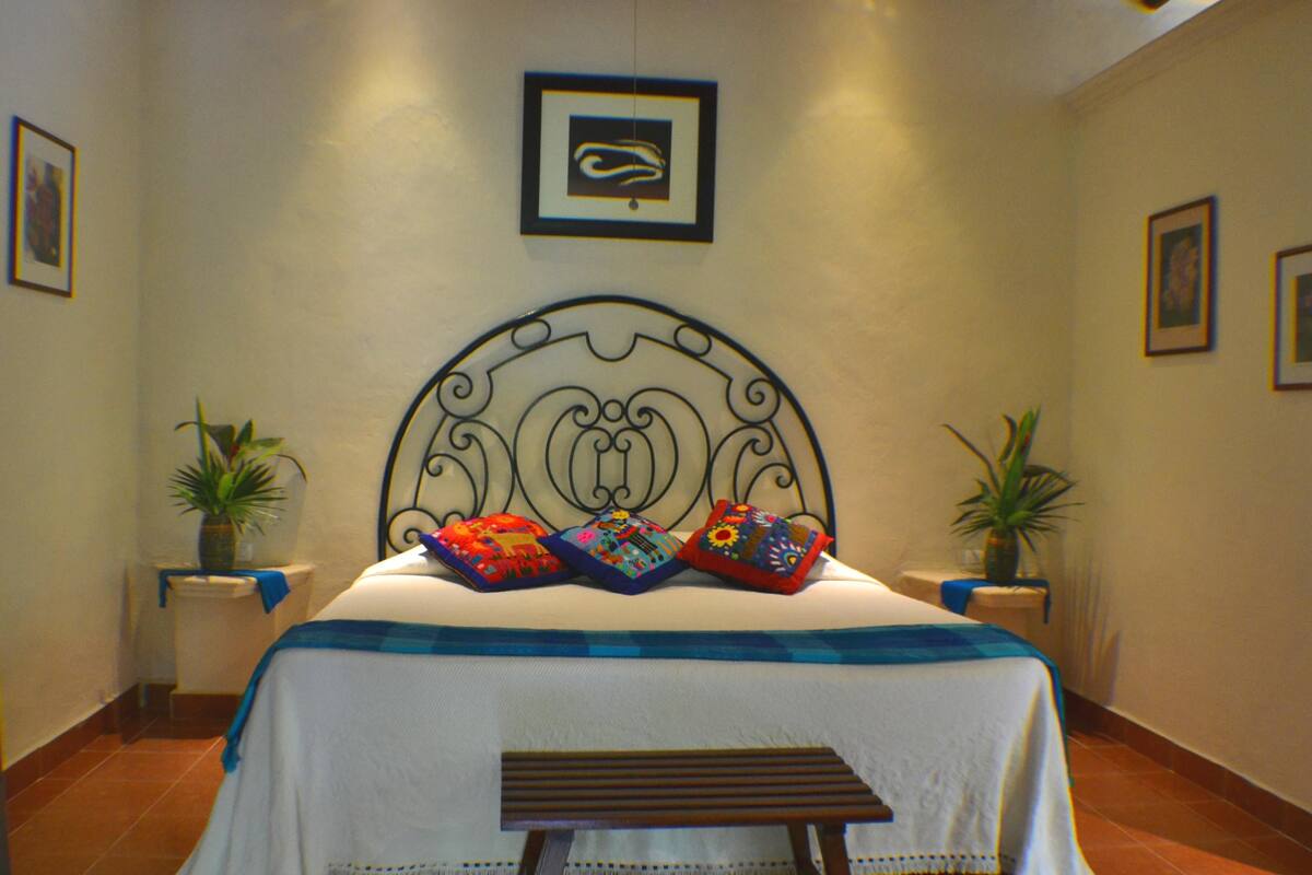 A neatly arranged bedroom with a bed, pillows, a bench, and two potted plants.