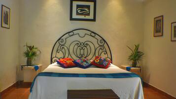 A neatly arranged bedroom with a bed, pillows, a bench, and two potted plants.