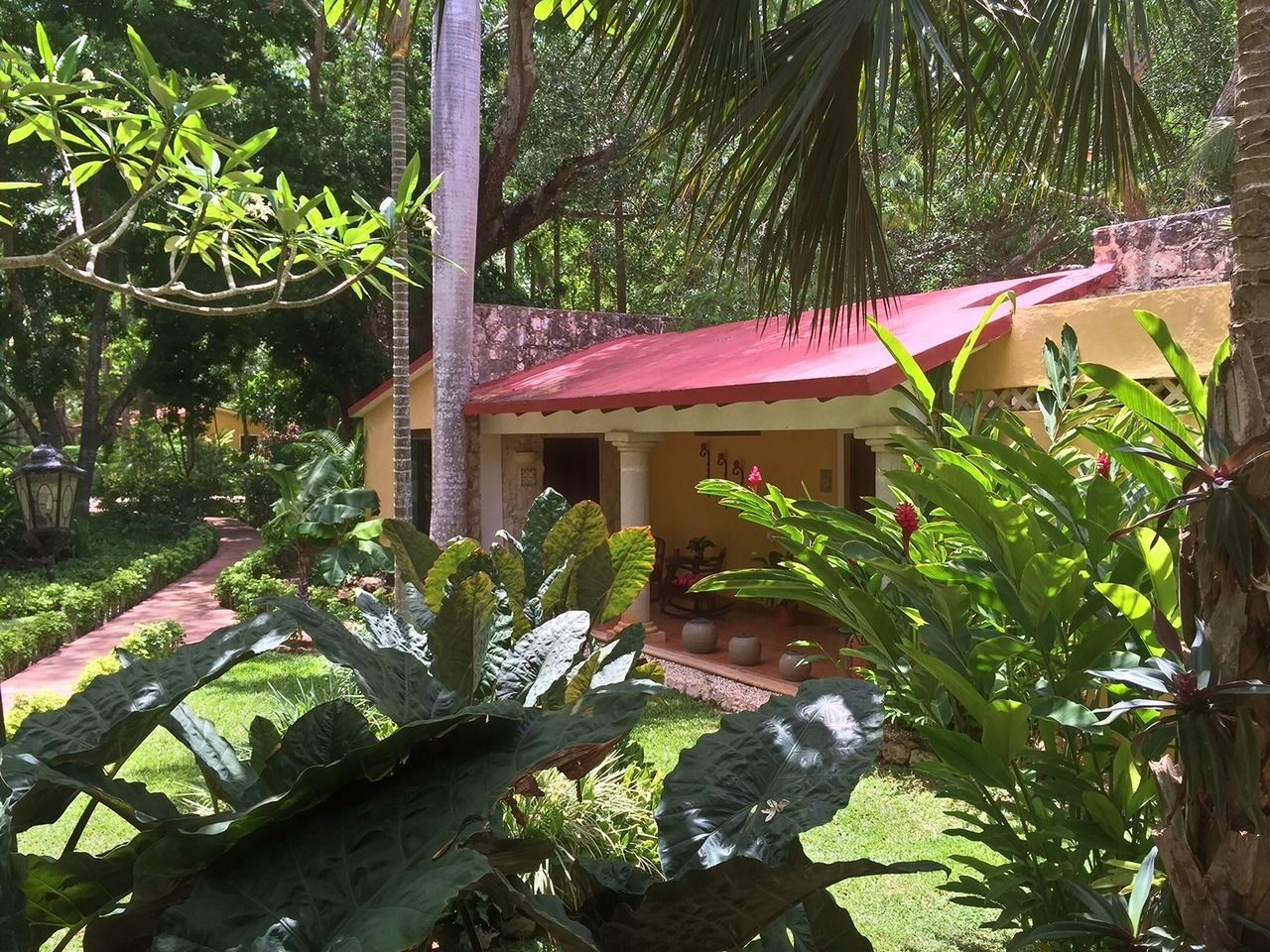 A yellow building with a red roof, surrounded by lush greenery and a pathway leading to it.