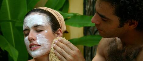 A person with a headband and another person applying a substance to their face.
