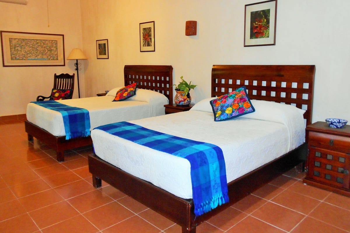 A hotel room with two single beds, a wooden nightstand, a chair, and a small table with a bowl.