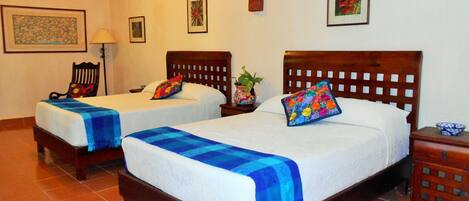 A hotel room with two single beds, a wooden nightstand, a chair, and a small table with a bowl.