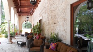 A covered patio area with wicker furniture, potted plants, and stone flooring. - Hacienda Chichen Resort & Yaxkin Spa (Chichen Itza)