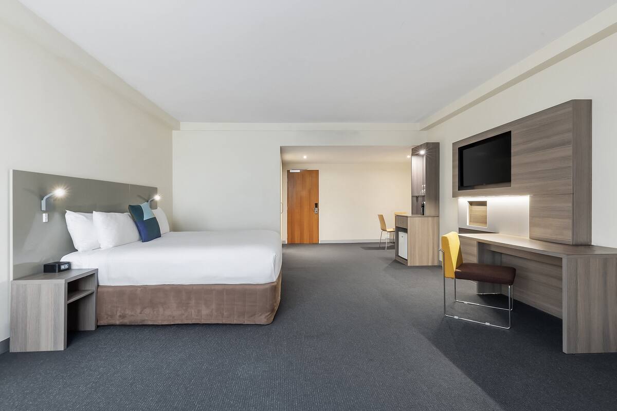 Een moderne hotelkamer met een groot bed, een bureau met stoel, een flatscreen-tv en een zithoekje.
