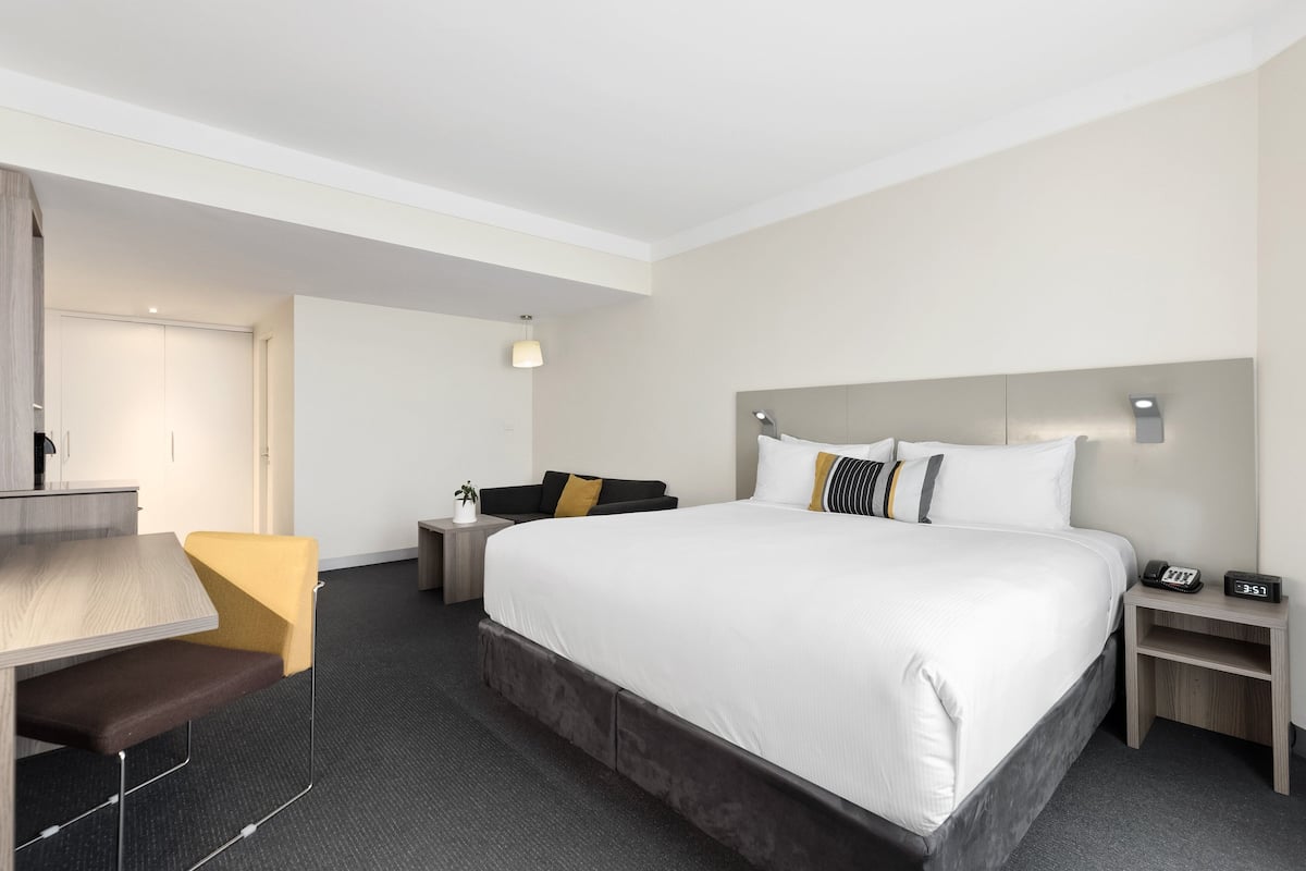 Een hotelkamer met een bed, een bureau, een stoel, een nachtkastje en een lamp.