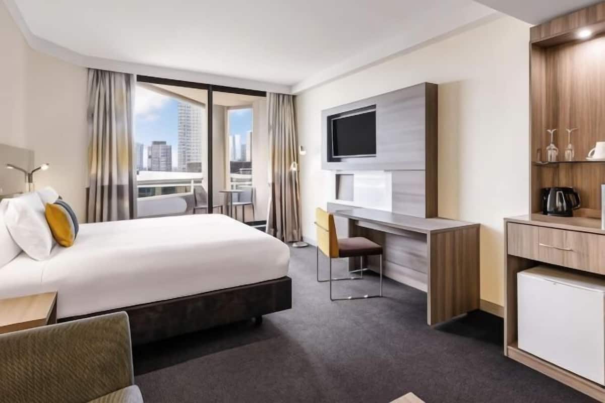 Een hotelkamer met een bed, bureau, stoel, televisie en uitzicht op de stad.