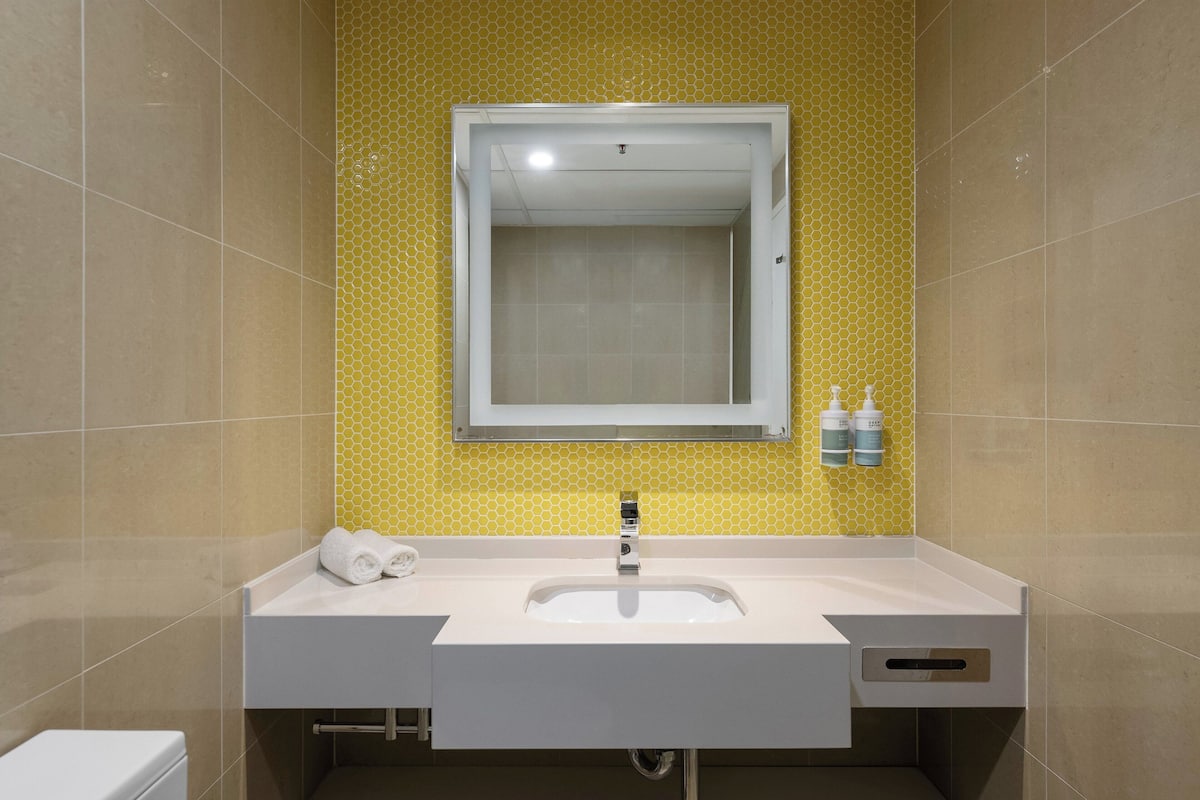 Een badkamer met een witte wastafel, een spiegel en een geel behang.