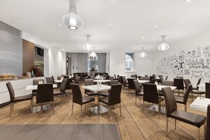 Un restaurante moderno con varias mesas y sillas, iluminación colgante y un mural en la pared.