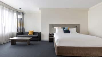 Una habitación de hotel con una cama grande, un sofá, una mesita de centro y una mesita de noche.