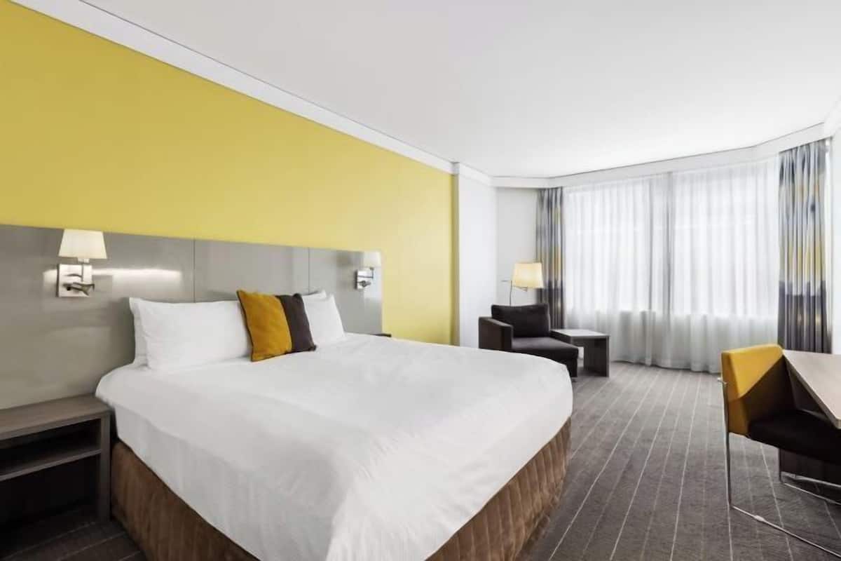 Een hotelkamer met een groot bed, een bureau, een stoel en een raam met gordijnen.