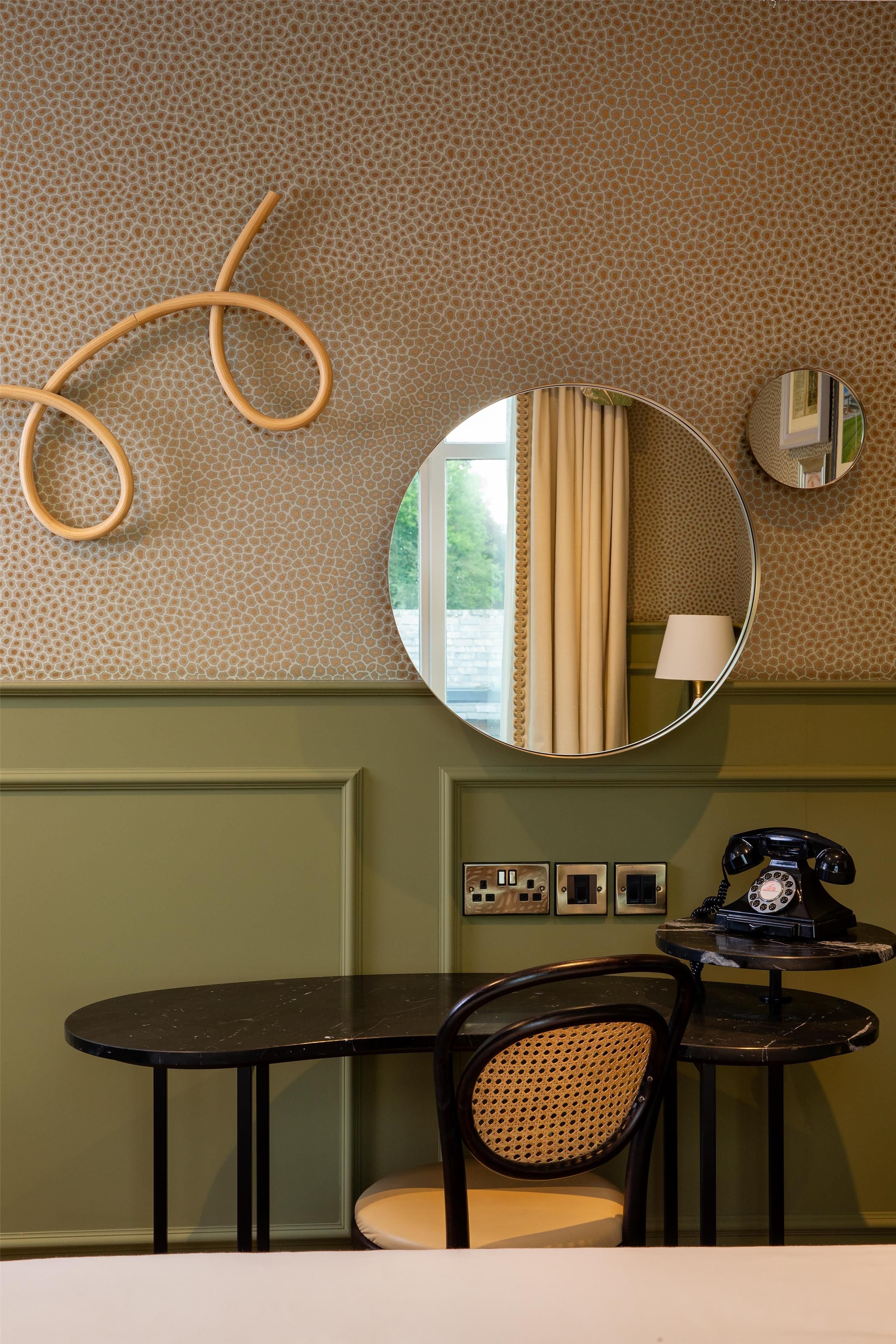 Una habitación con un espejo redondo, un teléfono y una mesa con una silla.