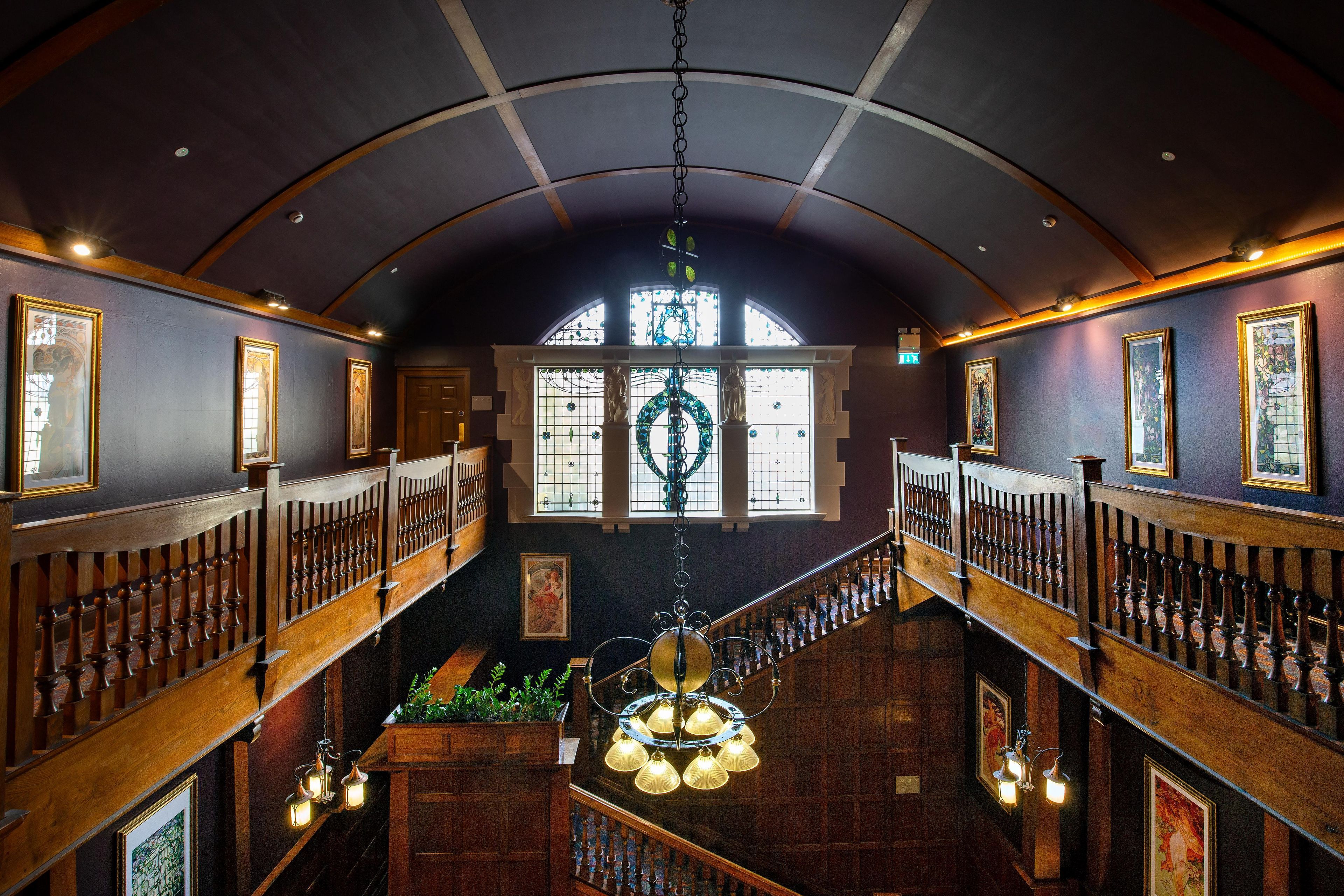 A grand interior with a high arched ceiling, wooden railings, and a central staircase.